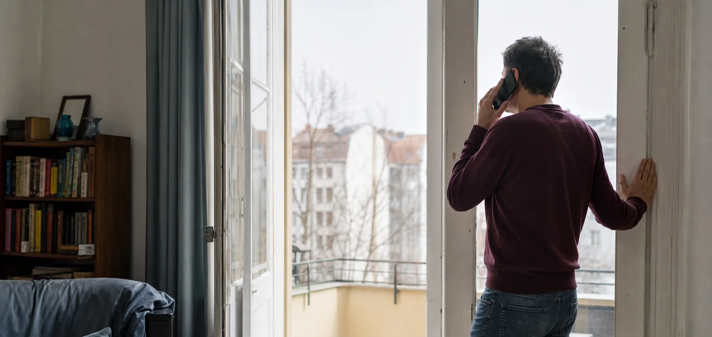 Otthonról telefonáló ember egy nyitott erkélyajtónál